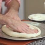 hand spreading pizza dough on pizza pan