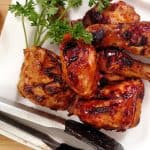 Indoor BBQ Chicken Grill on white plate with tongs, bbq sauce, parsley, bamboo cutting board