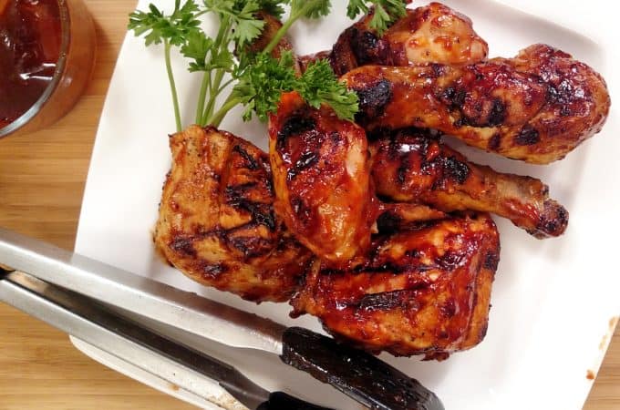 Indoor BBQ Chicken Grill on white plate with tongs, bbq sauce, parsley, bamboo cutting board