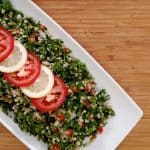 Tabouli salad, sliced lemon, sliced tomato on white plate on bamboo cutting board