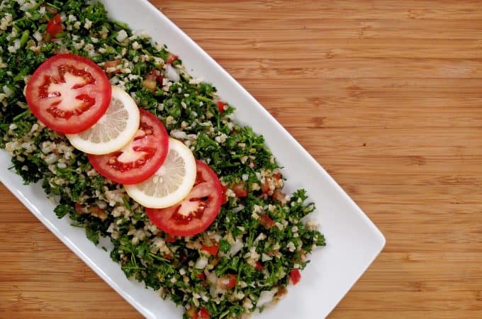 Tabouli salad, sliced lemon, sliced tomato on white plate on bamboo cutting board