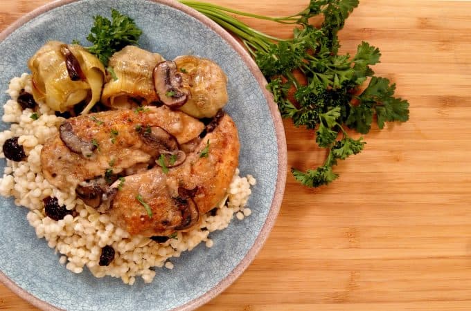 Chicken, Artichokes and mushrooms on a blue plate on bamboo cutting board with parsley