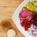 Italian Chopped Salad in a white bowl. pepperocini, salami, pepperoni, onions, cheese, garbanzo beans, roasted red peppers, Italian dressing