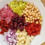 Italian Chopped Salad in a white bowl. pepperocini, salami, pepperoni, onions, cheese, garbanzo beans, roasted red peppers, Italian dressing