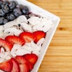 Red white blue acai bowl. blueberries, sliced strawberries, coconut flakes in white bowl on bamboo cutting board