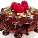 Flourless Chocolate Cake with Ganache, chopped nuts and raspberries on a white plate