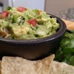 Guacamole in a black bowl with chips