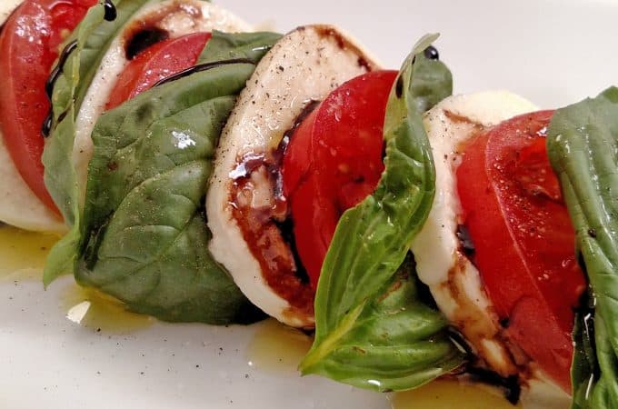 Caprese Salad, mozzarella, tomatoes, basil with a Balsamic Glaze and olive oil on white plate