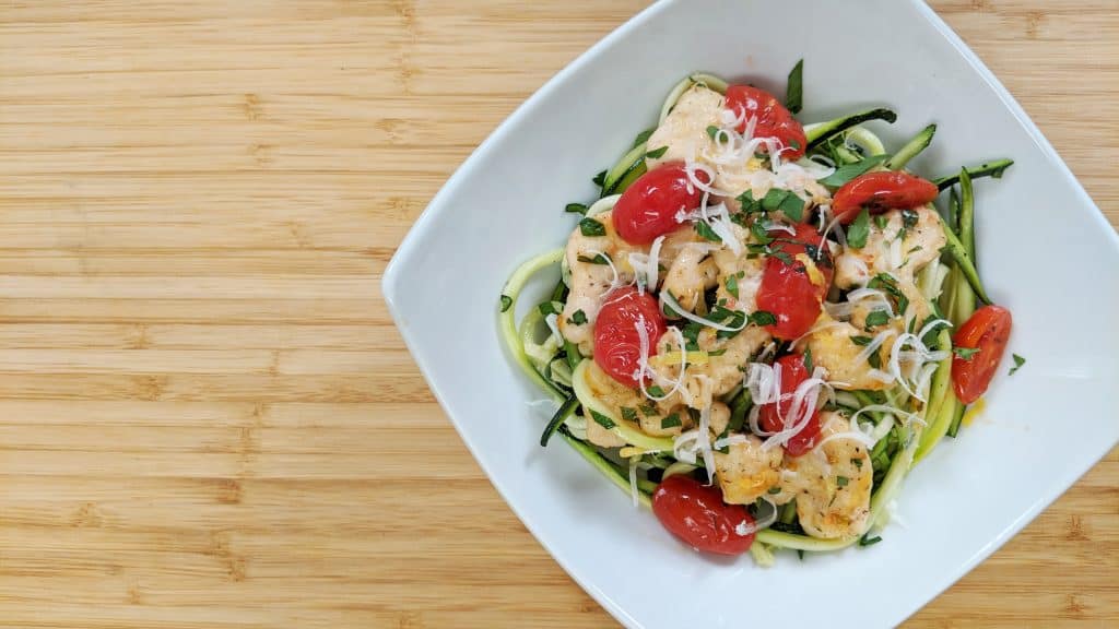 Zoodle Lemon Chicken with zoodles, tomatoes, lemon , chicken on white plate on bamboo cutting board