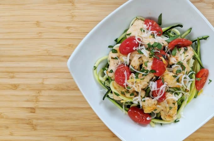 Zoodle Lemon Chicken with zoodles, tomatoes, lemon , chicken on white plate on bamboo cutting board