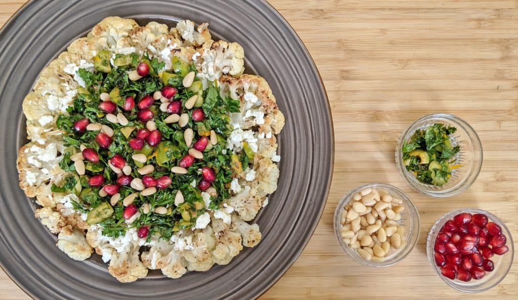Roasted Cauliflower with Parsley, pomegranate seeds, olives, mint and feta cheese on a brown plate