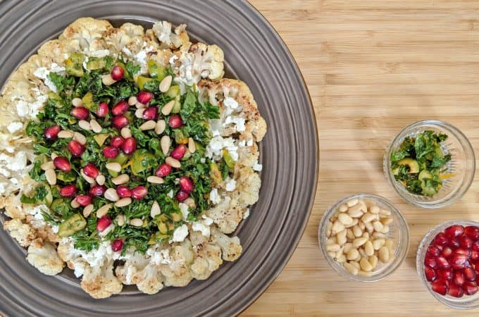 Roasted Cauliflower with Parsley, pomegranate seeds, olives, mint and feta cheese on a brown plate