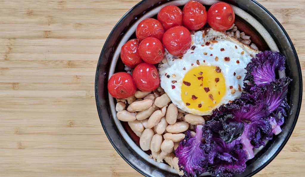 Farro Grain Bowl with Purple Kale, Cherry Tomatoes, Cannellini Bean and a Fried Egg with Red Pepper Flakes