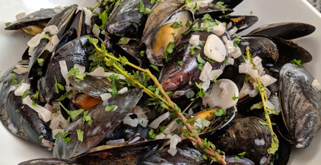A bowl of blue/black mussels with a crusty baguette. Classic French mussel recipe with Garlic, shallots and thyme flavor the dish.