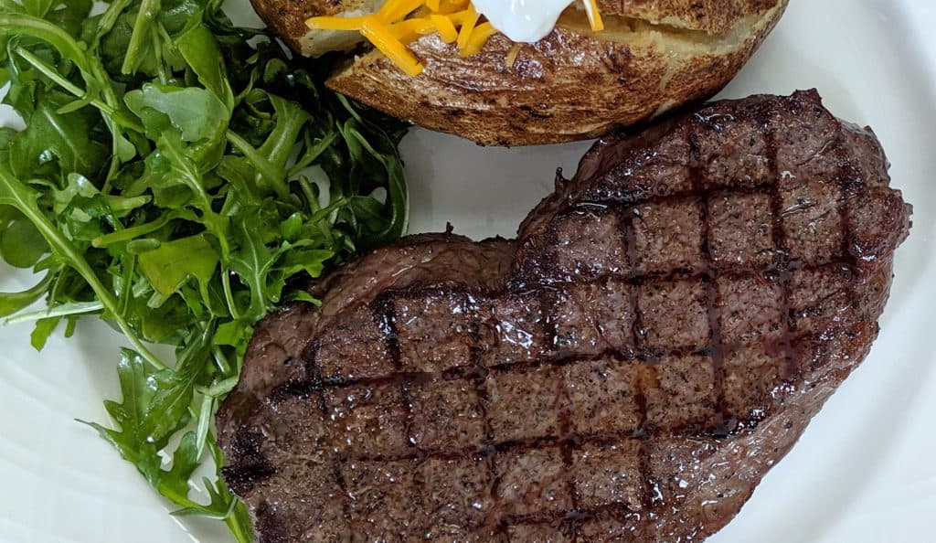 Steak with grill marks on a white place with a salad and baked potato