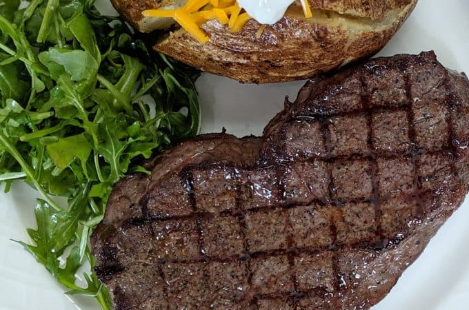 Steak with grill marks on a white place with a salad and baked potato