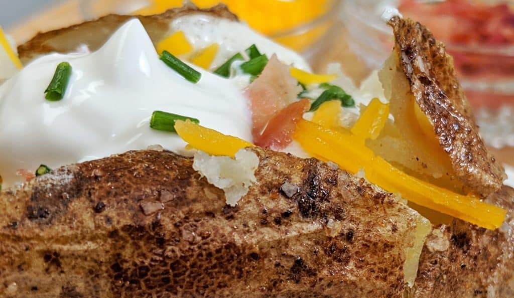 Close up of a baked potato with flaked salt chives, bacon, sour cream, butter and cheddar cheese