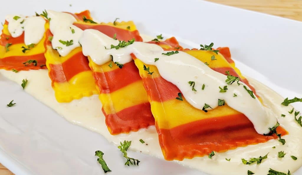 Red and Yellow Striped Lobster Ravioli with Cream Sauce plated on white plate with parsley