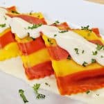 Red and Yellow Striped Lobster Ravioli with Cream Sauce plated on white plate with parsley