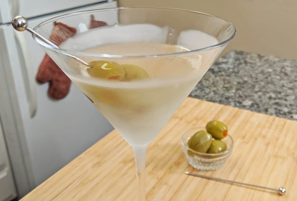 martini served in a frosted martini glass with olives on a bamboo cutting board