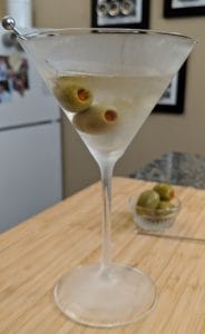 martini in a martini glas with olives on a wood cutting board