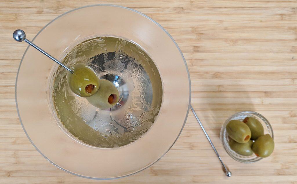 overhead view of a martini with olives on a bamboo cutting board