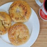 Overhead view of Keto Bagels with Sesame Seeds and Poppy Seeds and Sunflower Seeds on a white plate with a Tiny Kitchen Big Taste Coffee Mug