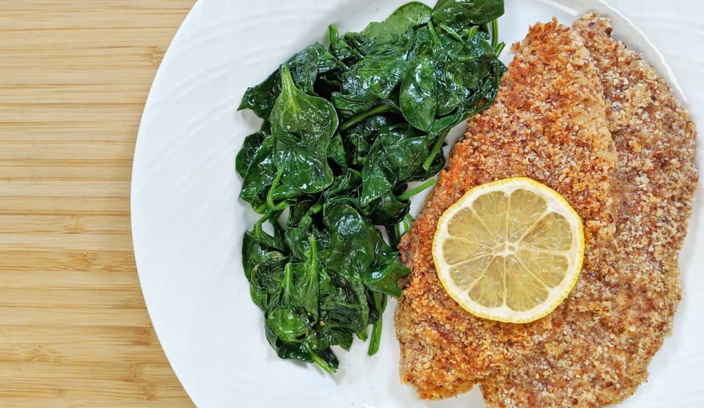 Tiny Kitchen Keto Almond Crusted Fish with lemon and wilted spinach on white plate and bamboo cutting board