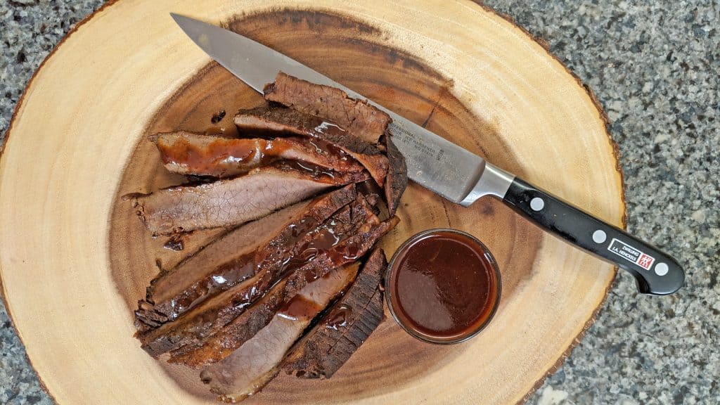 Sliced Brisket on cutting board with knife and bbq sauce