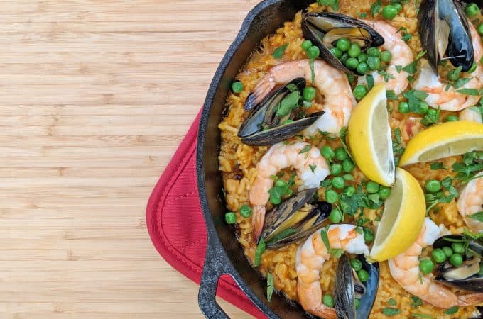 Paella with shrimp, mussels, saffron rice, peas and lemon in a black pan